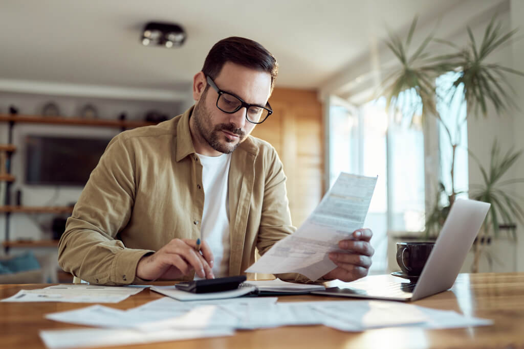 Young man using calculator while working on his financial plans at home.