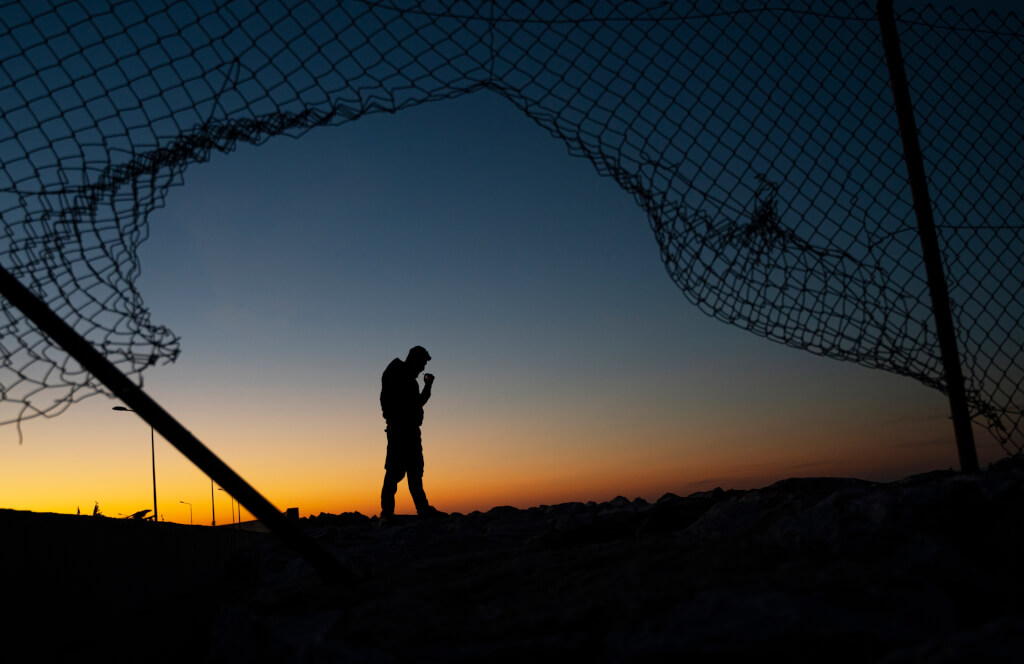 Refugee man standing behind the fence at sunrise