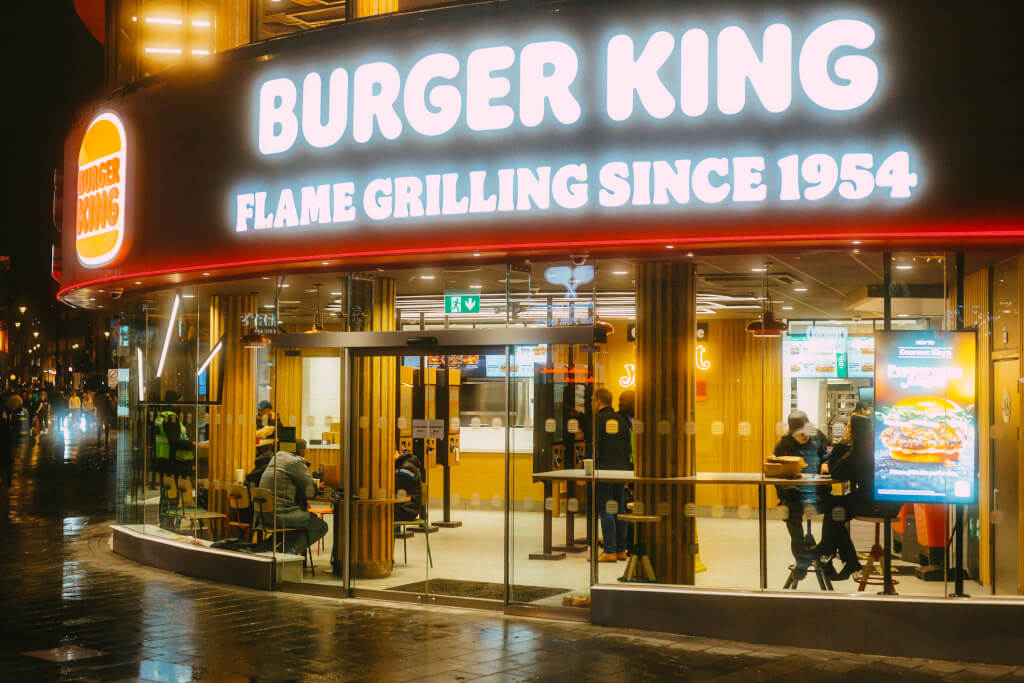 exterior architecture of a Burger King restaurant in Leicester Square, London, UK. It is night time and the restaurant is illuminated and customers are eating their food inside