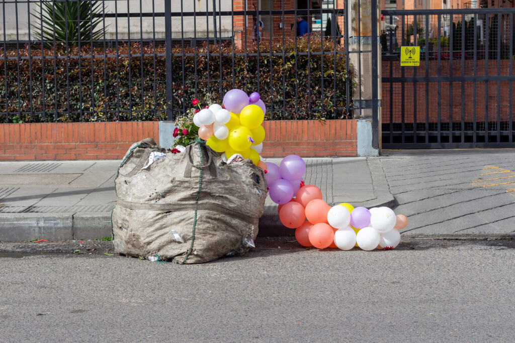 After a party, multicolor inflatable balls are dumped into a trash bag in the street. Bogota, San Jose de Bavaria, Colombia.