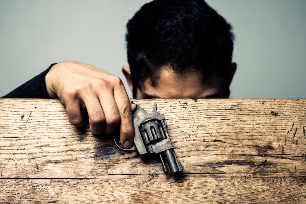 Student at school desk with gun detail. Student is opening an old school desk to look for something. He has a gun in his hand.