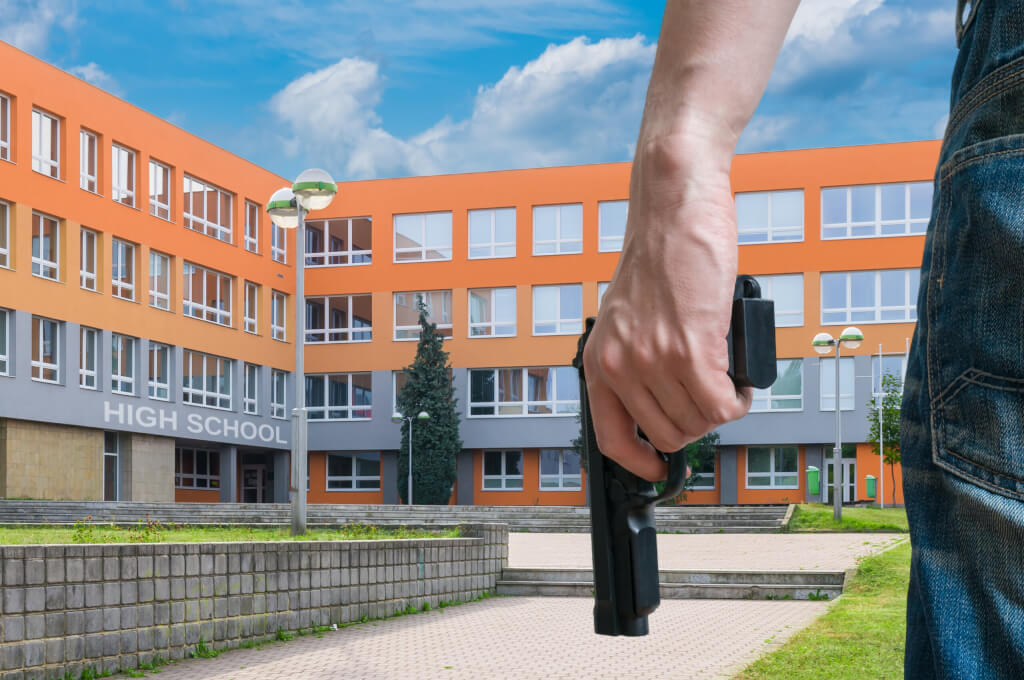 Gun control concept. Young armed man holds pistol in hand in public place near high school.